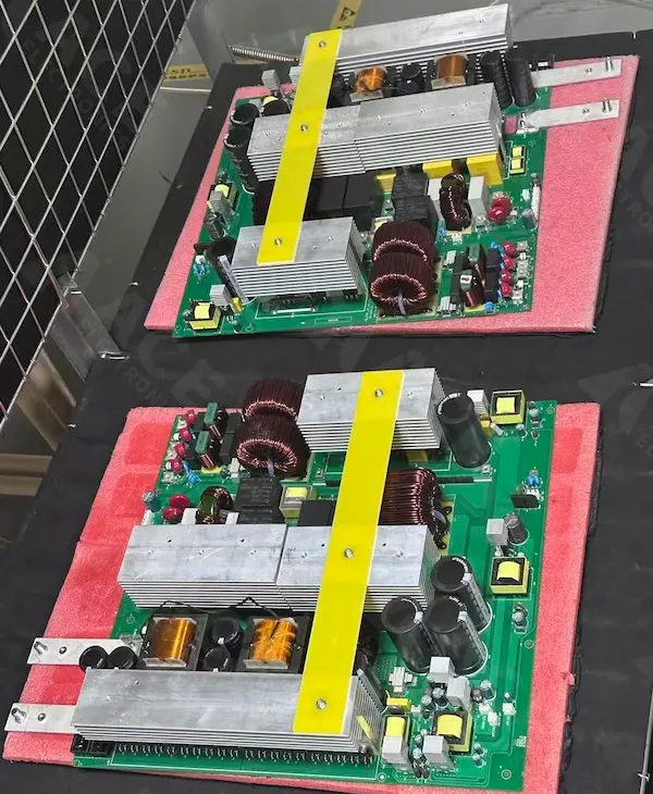 Top-side view of an industrial and commercial energy storage inverter power board with large aluminum heatsinks, copper-wound inductors, electrolytic capacitors, and an insulated yellow support bar used to stabilize the heatsink assembly.